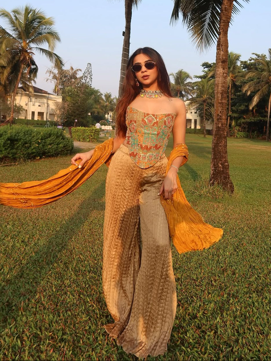 Woman in a traditional outfit with a yellow dupatta standing in a park with palm trees.